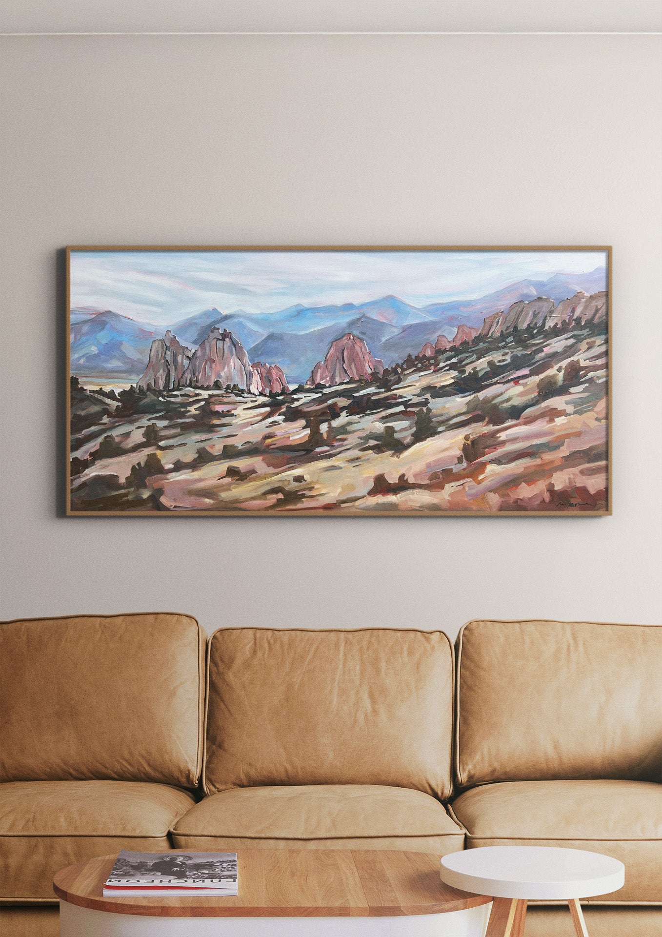 Painting of a mountain landscape above a beige sofa in a living room.